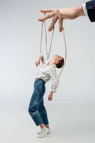 обрезанный вид кукловода, держащего марионетку на струнах, изолированных на сером
