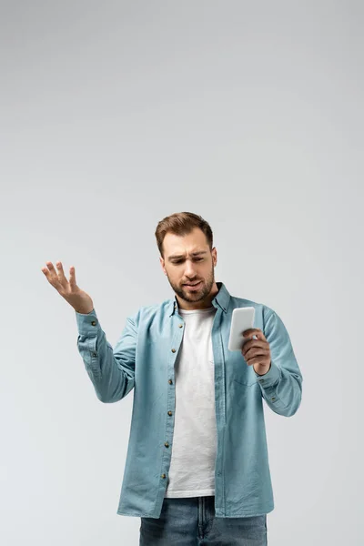 Verwarde Jonge Man Met Behulp Van Smartphone Geïsoleerd Grijs — Stockfoto