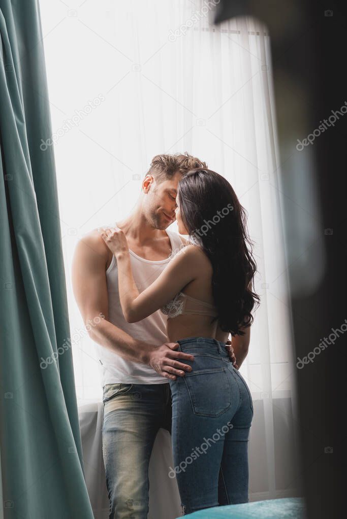Selective focus of sensual woman kissing boyfriend near window 