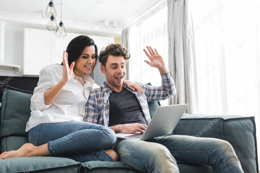 Smiling couple having video call on laptop in living room
