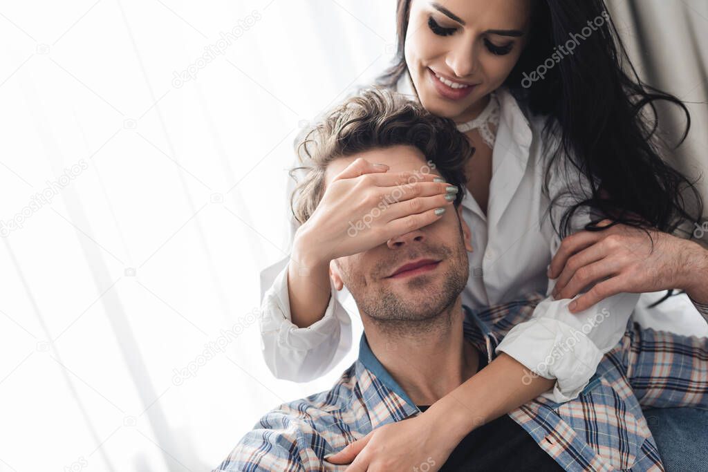 Smiling woman covering eyes to boyfriend on couch 