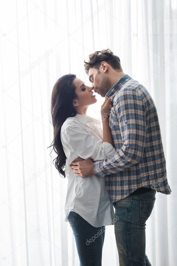 Handsome man kissing beautiful woman near window at home 