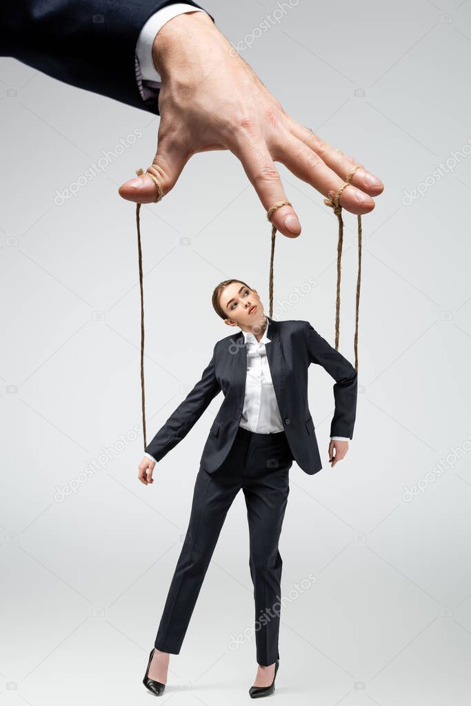 cropped view of puppeteer holding businesswoman marionette on strings isolated on grey