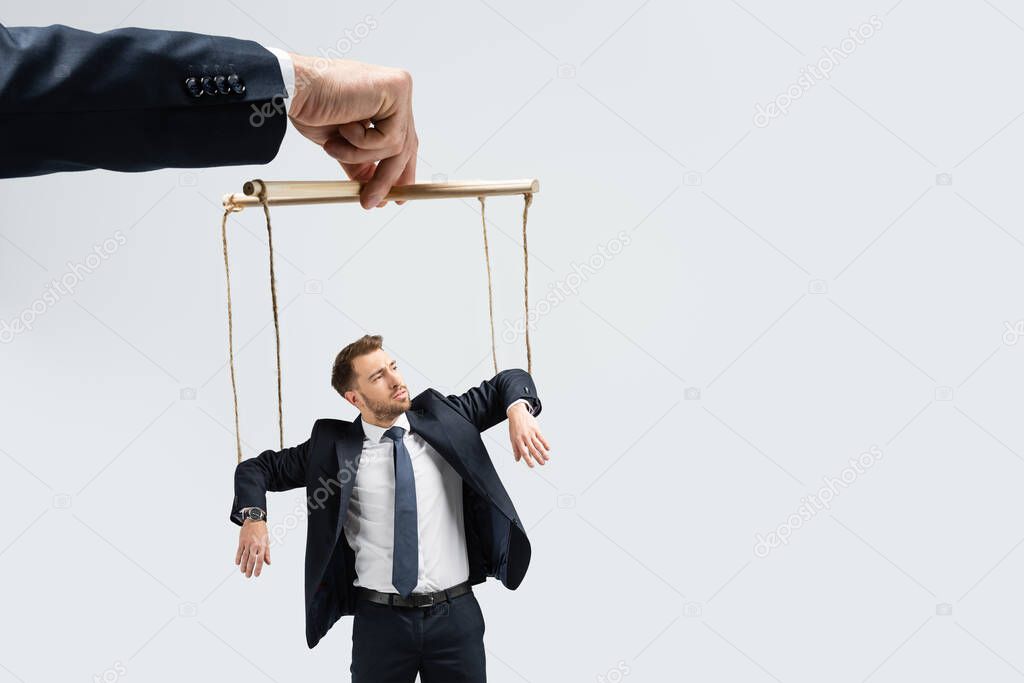 cropped view of puppeteer holding businessman marionette on strings isolated on grey