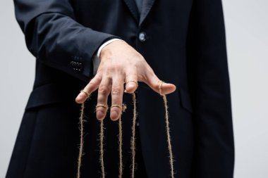 partial view of puppeteer in suit with strings on fingers isolated on grey clipart