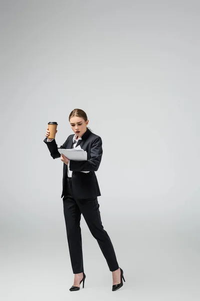 Šokovaná Mladá Podnikatelka Kávou Jít Papíry Izolované Šedé — Stock fotografie