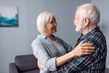 Mutlu yaşlı çift kucaklaşırken ve birbirlerine bakarken gülümsüyor.