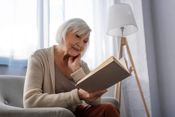 Mulher Sênior Positivo Sorrindo Enquanto Sentado Poltrona Livro Leitura — Fotografia de Stock