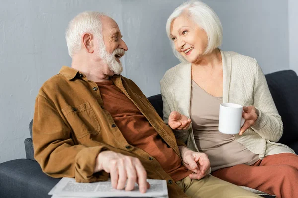 Alegre Anciana Sosteniendo Taza Mientras Habla Con Sonriente Marido — Foto de Stock