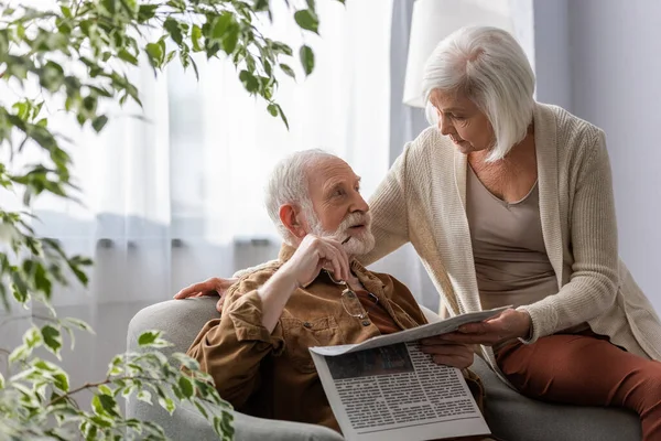 Senior Woman Talking Husband Holding Newspaper Eyeglasses While Sitting Armchair — Stock Photo, Image