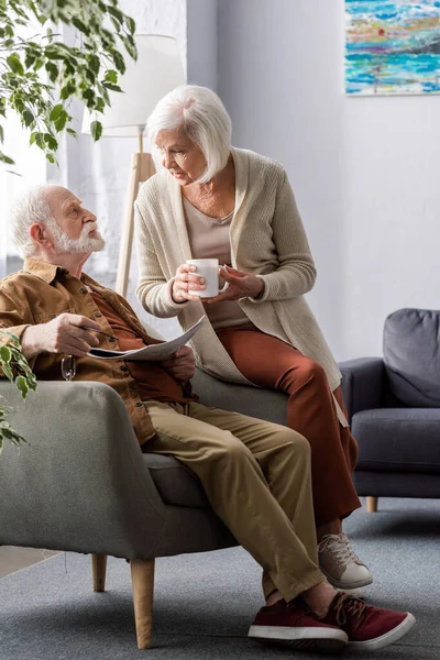 Пожилая Женщина Держит Чашку Чая Разговаривая Мужем Сидящим Кресле Газетой — стоковое фото