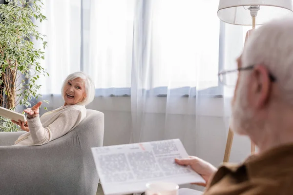Mujer Feliz Sentada Sillón Con Libro Mientras Habla Con Marido — Foto de Stock