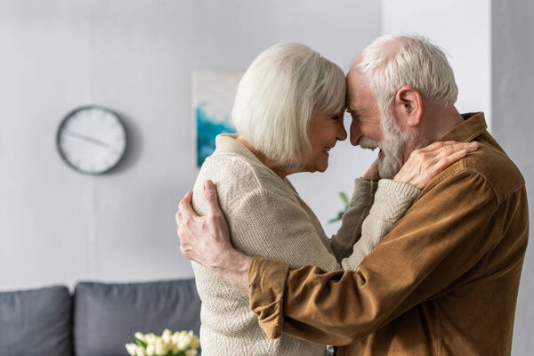 side view of happy senior couple embracing and laughing while standing face to face