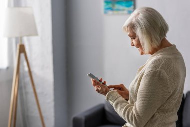 Evde akıllı telefon kullanan gülümseyen yaşlı kadının yan görüntüsü