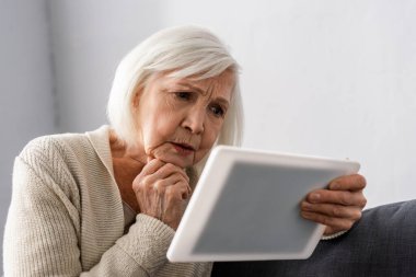 Dijital tablet kullanırken çenenin yanında el ele tutuşan endişeli yaşlı kadın