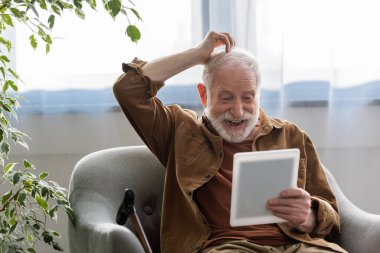 Neşeli kıdemli adam koltuğunda dijital tablet kullanırken dokundu.