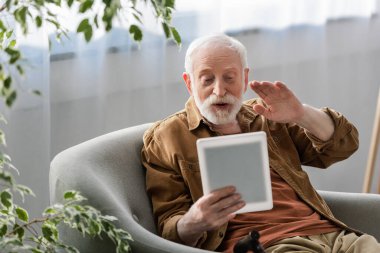 Dijital tablet üzerindeki video çağrısı sırasında el sallayan mutlu yaşlı adamın seçici odağı
