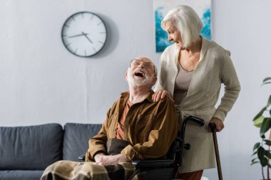 Kıdemli eş ve tekerlekli sandalyedeki neşeli koca birbirlerine bakıp gülüyorlar.