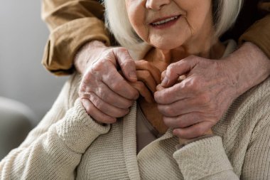 partial view of senior man holding hands of smiling wife clipart