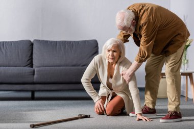 senior man helping wife sitting on floor near walking stick clipart
