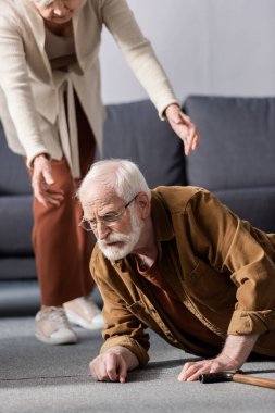 cropped view of woman helping fallen senior husband to get up from floor clipart