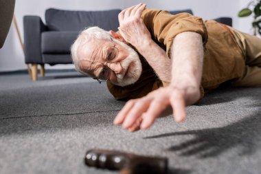selective focus of helpless senior man fallen on floor and trying to get walking stick clipart