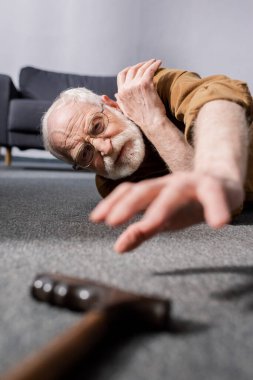 selective focus of powerless senior man lying on floor and trying to get walking stick clipart