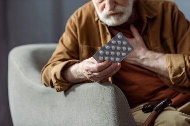 selective focus of senior man touching chest and holding pills while feeling bad clipart