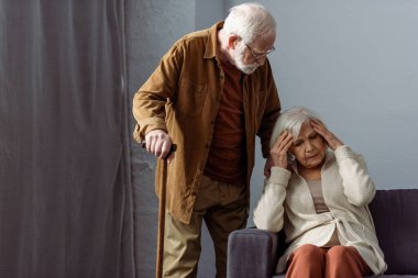 Elinde baston olan son sınıf öğrencisi, karısının yanında duruyor ve Hedache 'den acı çekiyor. 