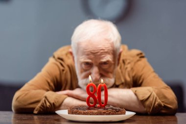 selective focus of lonely senior man looking at birthday cake with number eighty clipart