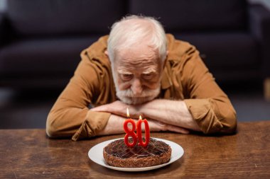 lonely senior man looking at birthday cake with number eighty clipart