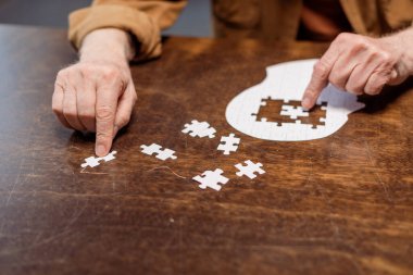 partial view of senior man playing jigsaw puzzle as dementia therapy clipart