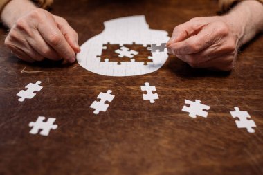cropped view of ill senior man collecting jigsaw puzzle for dementia therapy clipart