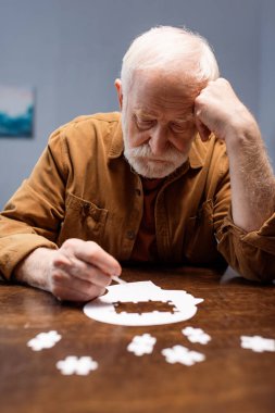 selective focus of senior man collecting jigsaw puzzle as dementia therapy clipart