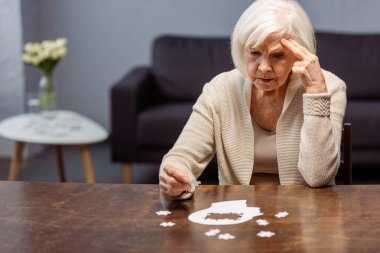 thoughtful senior woman collecting jigsaw puzzle as dementia therapy clipart
