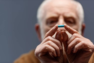 selective focus of senior man looking at pill in his hands clipart