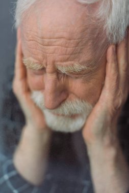 selective focus of senior, depressed man with closed eyes touching face near window glass clipart