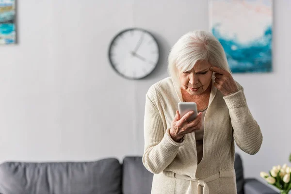 Στοχαστική Ηλικιωμένη Γυναίκα Που Αγγίζει Κεφάλι Ενώ Χρησιμοποιεί Smartphone — Φωτογραφία Αρχείου