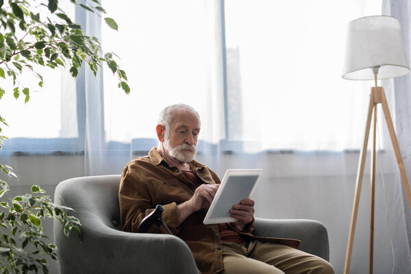 концентрированный пожилой человек с помощью цифрового планшета, сидя в кресле
