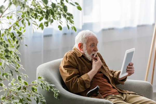 Chockad Senior Man Använder Digitala Surfplatta Medan Sitter Fåtölj — Stockfoto