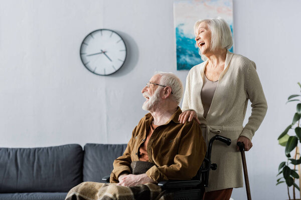 senior woman and handicapped husband in wheelchair laughing while looking away