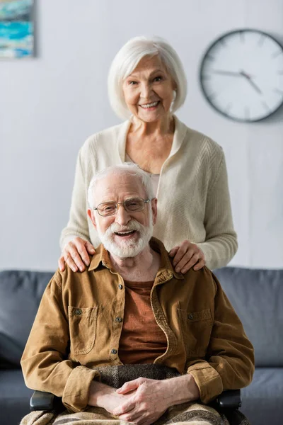 Happy Senior Woman Touching Shoulders Smiling Husband Sitting Wheelchair — Stock Photo, Image
