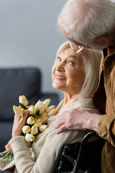 Счастливая Пожилая Женщина Инвалид Букетом Свежих Тюльпанов Смотрящая Мужа Трогающего — стоковое фото