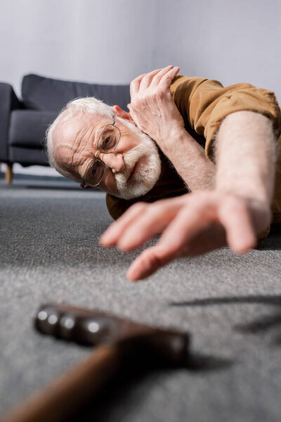 selective focus of powerless senior man lying on floor and trying to get walking stick
