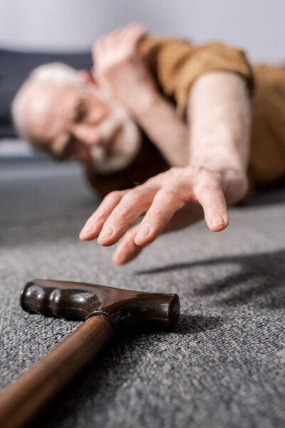 selective focus of helpless senior man lying on floor and trying to get walking stick