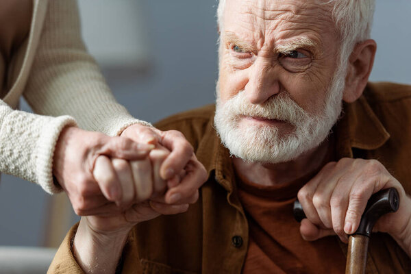 partial view of woman holding hand of senior husband, sick on dementia