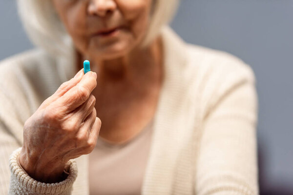 cropped view of senior woman holding pill, selective focus