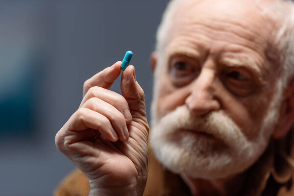 селективный фокус пожилого человека, смотрящего на таблетку в руке
