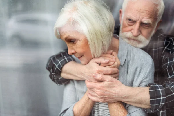 Upset Senior Man Hugging Wife Sick Dementia While Standing Window — Stock Photo, Image