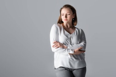 thoughtful, beautiful overweight girl standing with crossed arms isolated on grey clipart